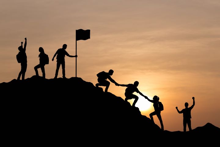 An Image of Several People Helping Each Other to the Top of a Mountain Representing Teamwork