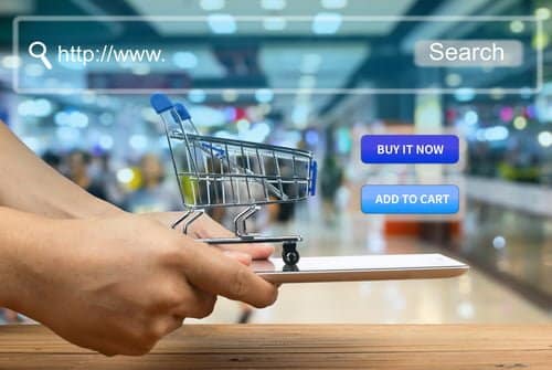 Picture of a Hands Holding a Shopping Cart with a Retail Store in the Background Representing an Online Shopping Cart